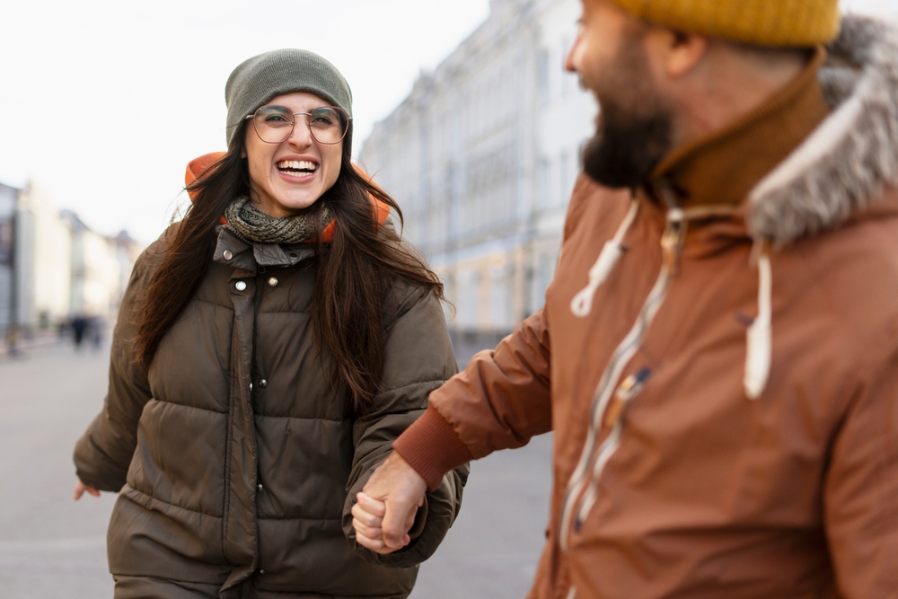 A couple knows What to Wear in Italy in December: the gentleman grabs his partner's hand and she wears a beanie, a scarf and a parka.