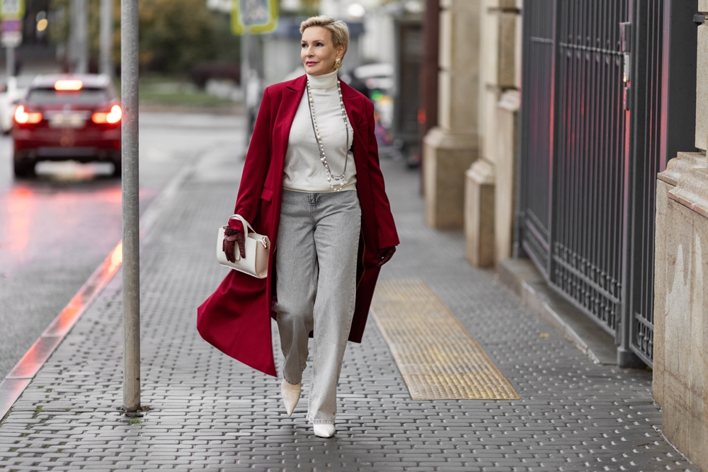 A woman in jeans, a turtleneck, and a red overcoat struts down the streets of NYC.
