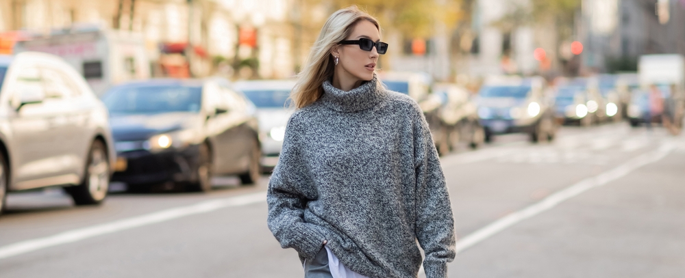 A woman enjoys the rare sunny days of December in NYC, knowing what to wear in New York City in December in her turtleneck, thick sweater.