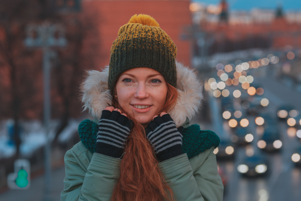 A woman pulls up her fur hood on her parka, gloves and beanie already attempting to keep her warm.