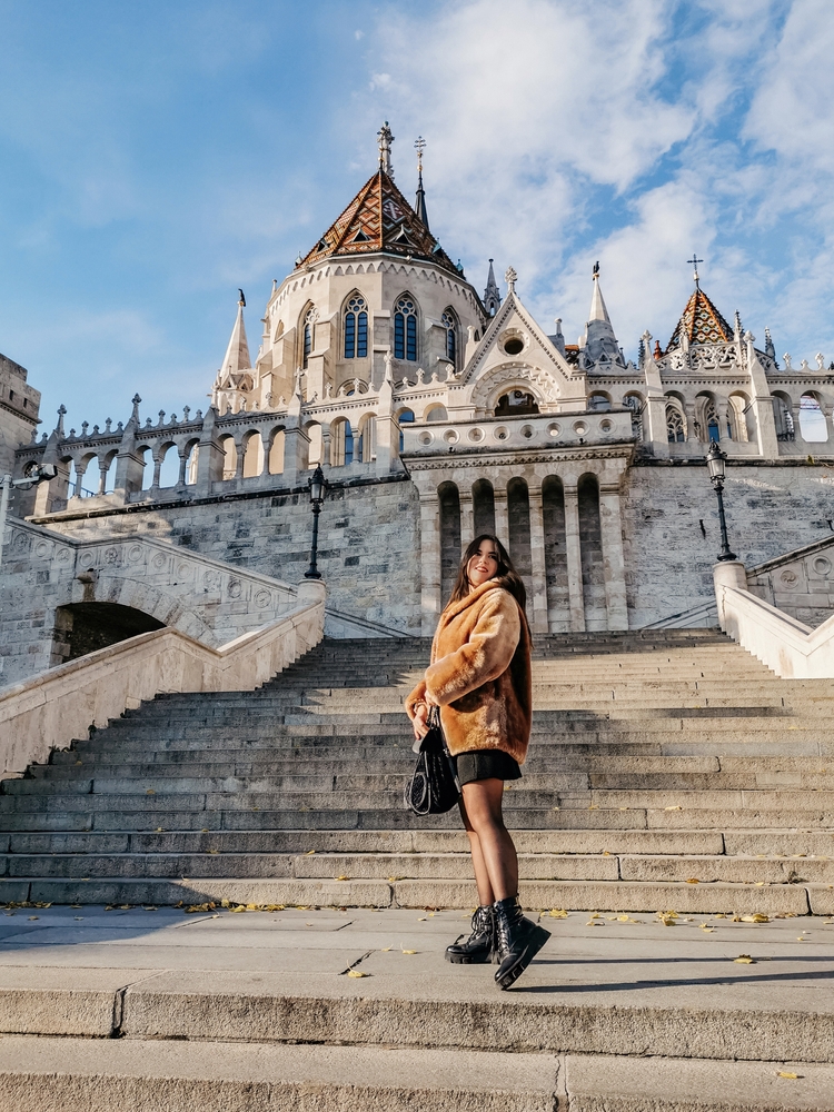 a woman is standing on a large set of stairs, she is wearing chunky boots, a short skirt, and a fuzzy jacket, budapest outfits