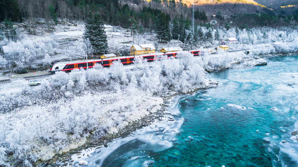 Train Oslo in the Bergen in mountains as it passes snow covered trees and an iced over lake during wintertime