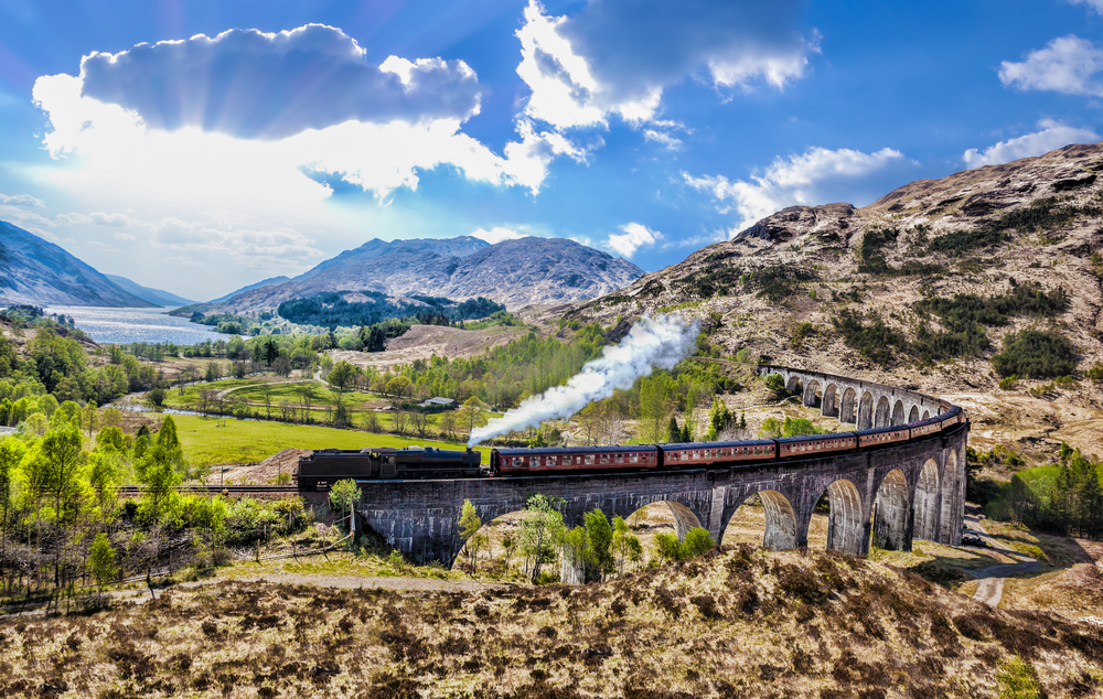 Glenfinnan Railway Viaduct in Scotland with the Jacobite steam train against sunset over lake on the Scottish Highlands Train route