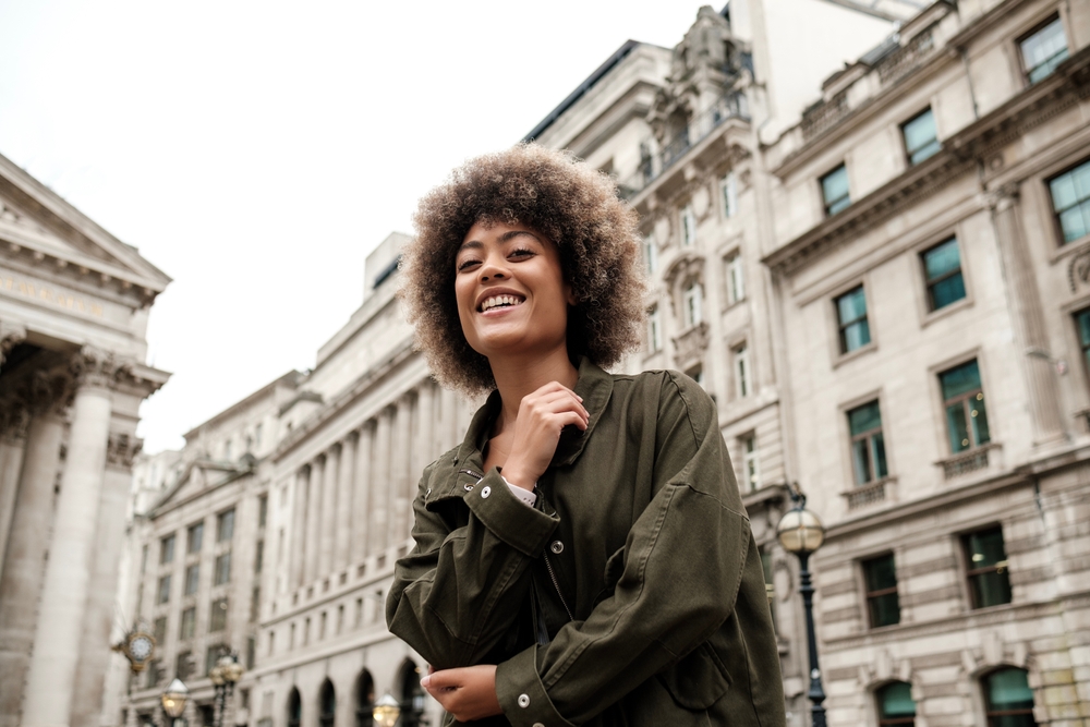 A young woman looks down at the camera her her olive green army jacket that keeps her warm during the fall.