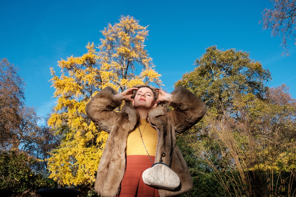 A woman runs her fingers through her hair: she knows what to wear in London in November with her midi dress and faux fur coat!