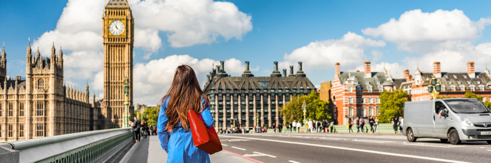 A woman knows what to wear in London in November on those sunnier days: she walks toward Big Ben with her blue jacket and red bag.