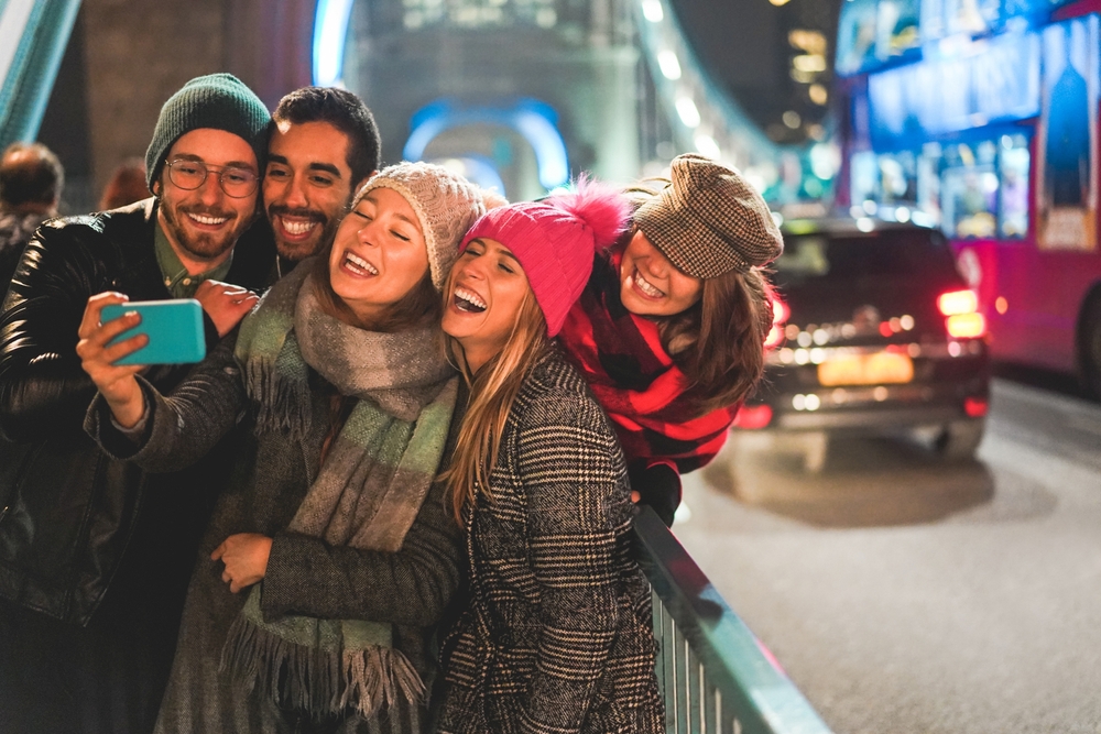 A group of friends smile for a photo on the Tower Bridge, all in wool jackets and hats and scarves for those colder nights.