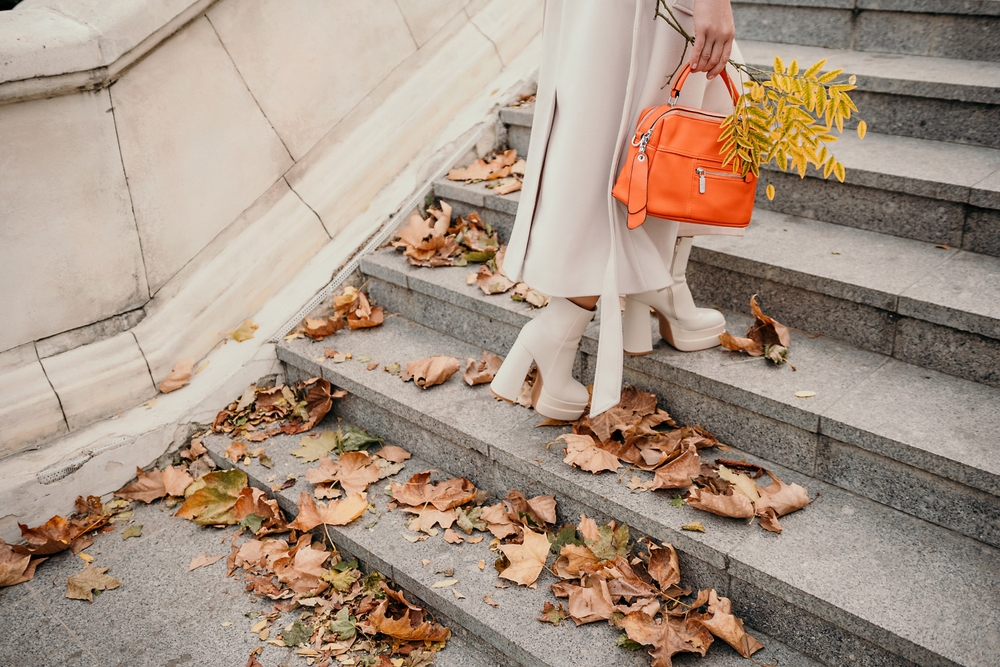 A woman climbs some stairs in NYC, her tan boots matching her long tan skirt: these shows are comfortable, waterproof and cute, showing she knows what to wear in New York City in November.