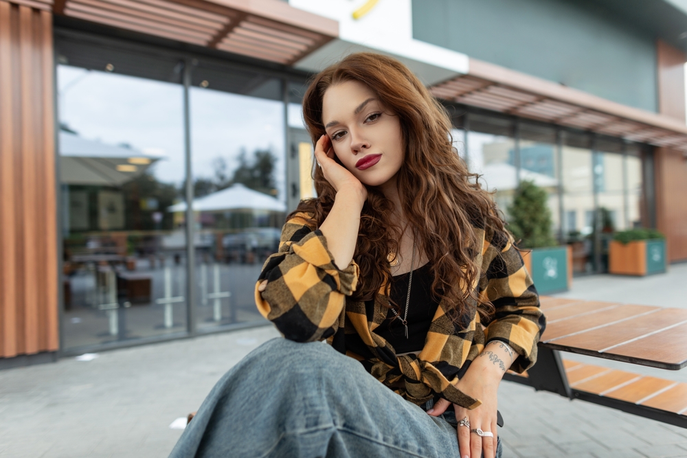 A young girl poses in NYC, knowing what to wear in New York City in November, in her straight leg jeans, flannel shirt, and more.