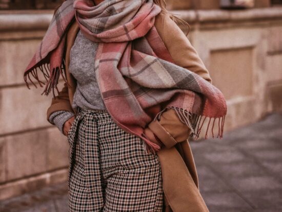 A close up shot of a woman who knows what to wear in New York City in November shows her plaid pants, thick turtle neck, beige jacket and plaid scarf: all fall colors and on theme too!