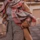 A close up shot of a woman who knows what to wear in New York City in November shows her plaid pants, thick turtle neck, beige jacket and plaid scarf: all fall colors and on theme too!