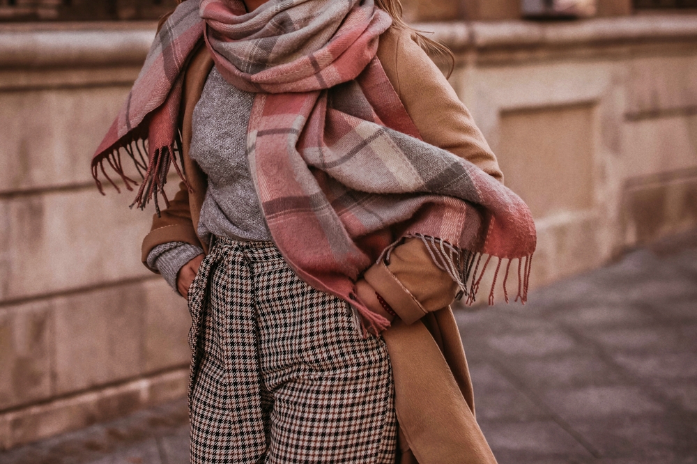 A close up shot of a woman shows her plaid pants, turtleneck, beige sweater and scarf.