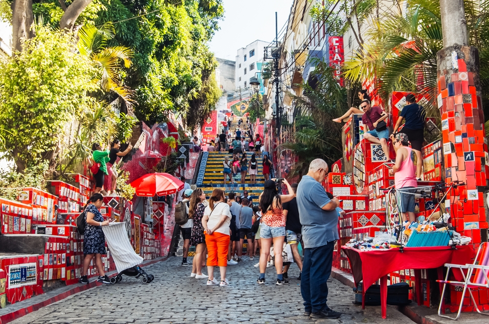 people standing in a busy street, there are stairs in the back, and street vendors on both sides of the street 