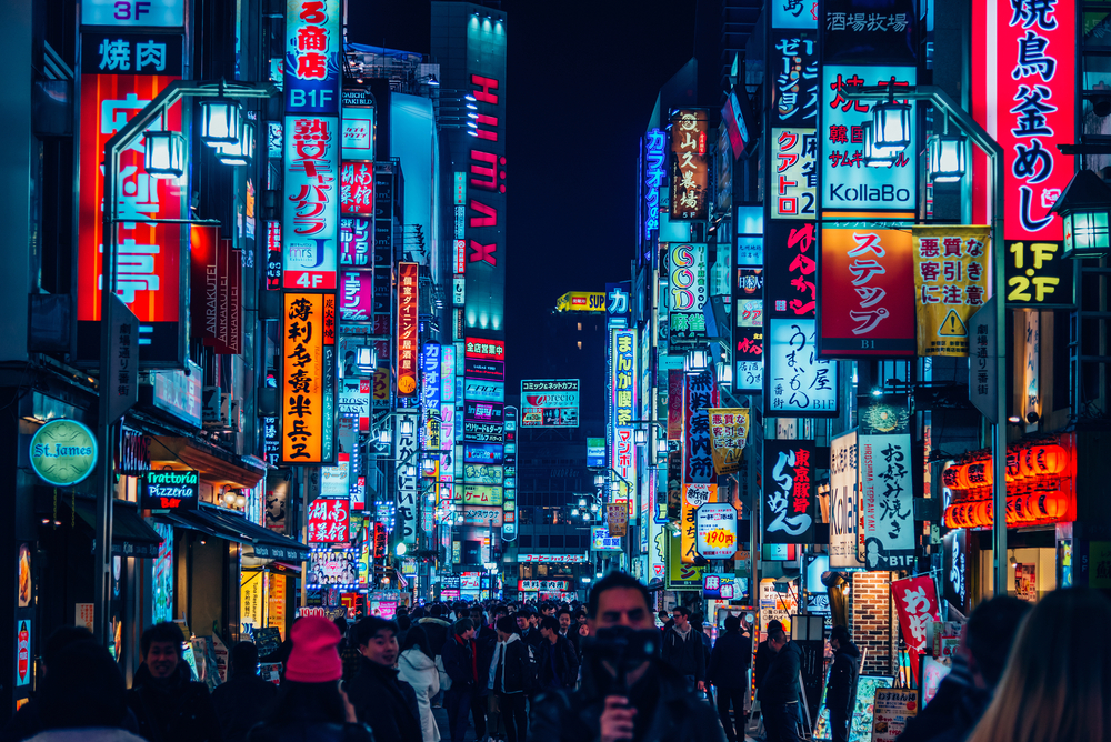 neon signs on both sides of a street in japan, there are a lot of people walking on the street and it is very crowded