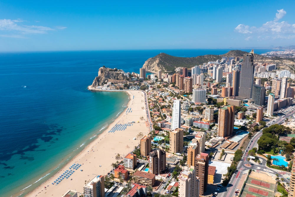 aerial photo of ocean, beach, and city. the buildings are on the right and the water on the left, it is a clear sunny day 