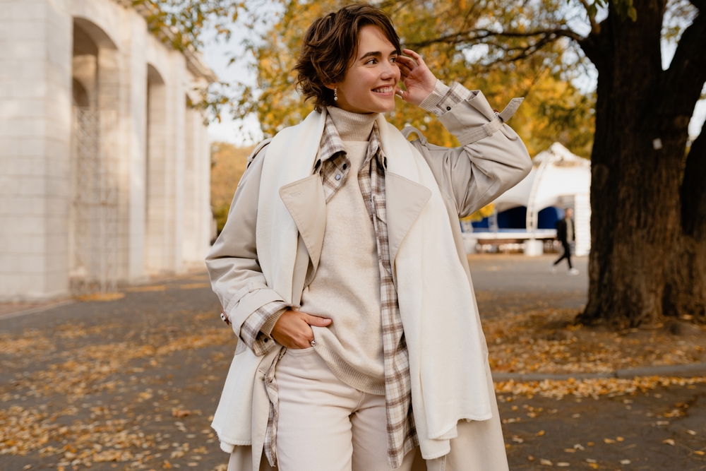 a woman in neutral creme color pallet with scarf, sweater, coat smiling during fall