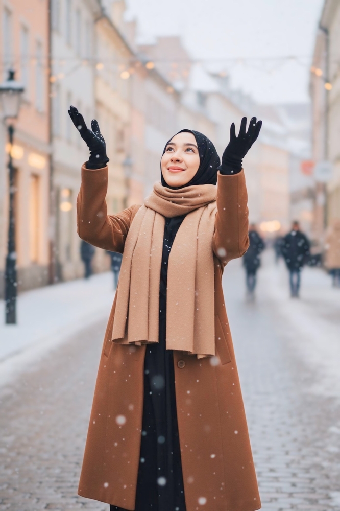 a woman dressed in neutrals with coat, gloves, scarf with snow in the city