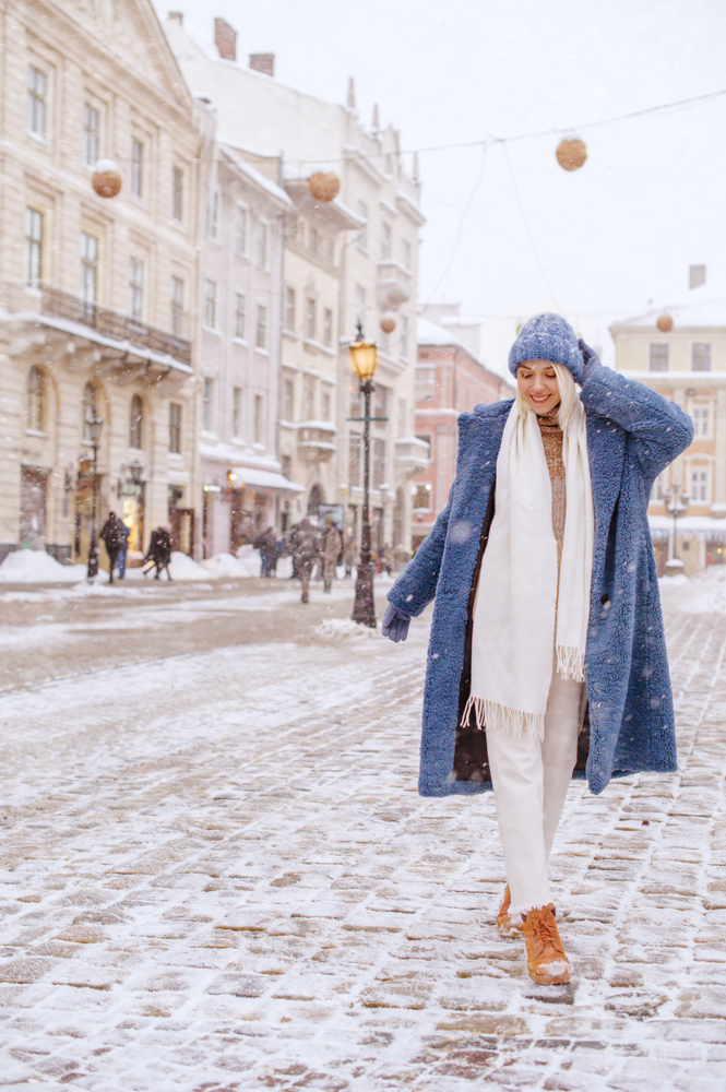 a woman in blue hat and blue coat in snow in europe with boots