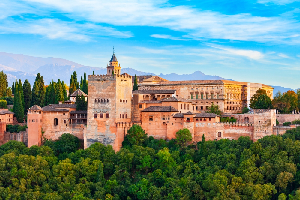In Andalusia, trees meet the edge of a famous pastel building: the Mequita. Mountains hover in the distance and the sky is blue. 