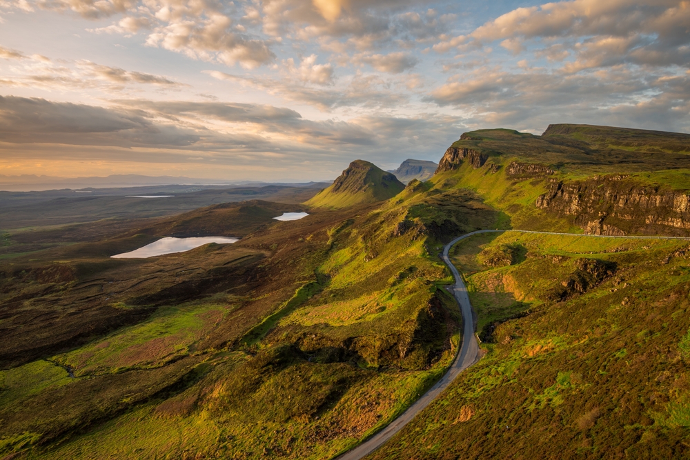 A spiral road twists and turns at dusk in Scotland: clouds are soft in the sky, and greens and browns stretch endlessly. 