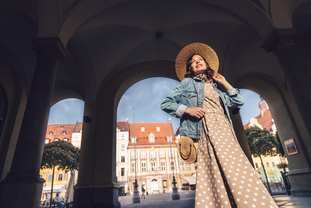 a woman posing in a dress, with jean jacket and purse posing for pictures in Europe