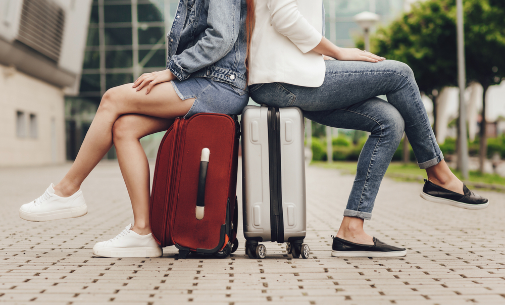 two women sitting on suitcases one with white sneakers and one with leather loafers