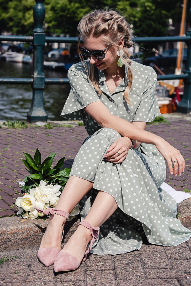 a woman sitting in front of canal with flowy dress and ballet flats